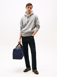 Hoodie cinza de algodão com um bolso frontal, cordões brancos, jeans azul escuro, sapatos de couro pretos e uma mala de lona azul com detalhes pretos.
