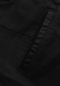 Tissu noir avec texture visible et surface lisse, comportant une poche avec un bord cousu et un design épuré.