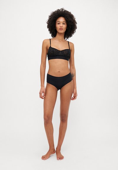 Conjunto de lencería negra que incluye un sujetador de puntos transparentes con tirantes ajustables y unas braguitas altas a juego, ambas en un material suave.