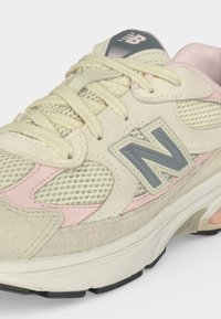 Μπεζ και ροζ αθλητικά παπούτσια New Balance με λεπτομέρειες από δίχτυ και καστόρι, εκρού κορδόνια και γκρι λογότυπο "N" στο πλάι.