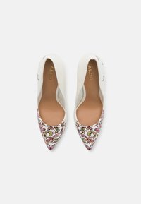 Ballerines blanches à gros orteils pointus avec un motif de papillon sur la zone des orteils. Matériau supérieur lisse avec une semelle intérieure beige et une marque dorée.