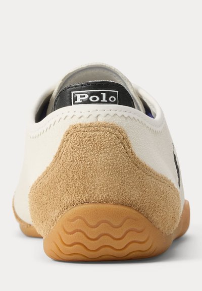 Vue arrière d'une basket blanche et beige avec une semelle en caoutchouc et une étiquette noire "Polo" sur le col du talon.