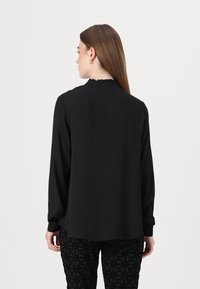 Zwarte blouse met lange mouwen en een gerimpelde kraag, van een gladde stof en met een losse pasvorm. Draagt goed met zwart, met textuur en patroon.