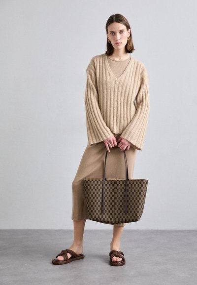 Beige ribbed sweater with wide sleeves, paired with a beige knee-length dress, brown checkered tote bag, and brown knotted sandals.