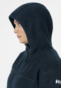 Marine fleece hoodie met een gestructureerde afwerking, volledige rits en capuchon. Beschikt over contrasterende afwerking langs de rits en schoudernaden.