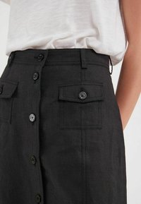 Jupe en lin noir avec des boutons sur le devant, deux poches plaquées et une taille ajustée. Le tissu texturé améliore l'apparence de profondeur et de structure.