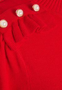 Red knitted sweater featuring a ribbed neckline, three gold-accented buttons, and a textured ruffle detail near the chest area.