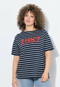 Camiseta de rayas azul marino con mangas cortas, que presenta rayas horizontales blancas y un destacado gráfico rojo "1987" en la parte frontal.