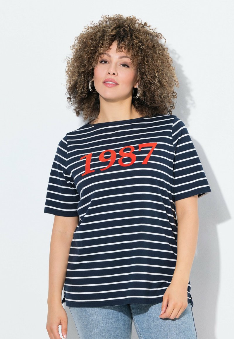 Camiseta de rayas azul marino con mangas cortas, que presenta rayas horizontales blancas y un destacado gráfico rojo "1987" en la parte frontal.
