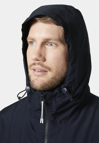 Marineblauwe hoodie met ritssluiting, verstelbare trekkoorden en textiel stof. Heeft een hoge kraag en zichtbare stikdetails.
