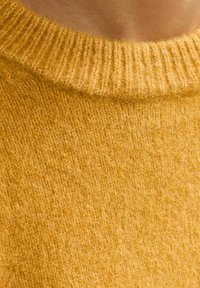 Mosterdgele trui met een geribde halslijn en een zachte, fuzzy textuur. De stof lijkt dik en comfortabel, geschikt voor koelere weersomstandigheden.