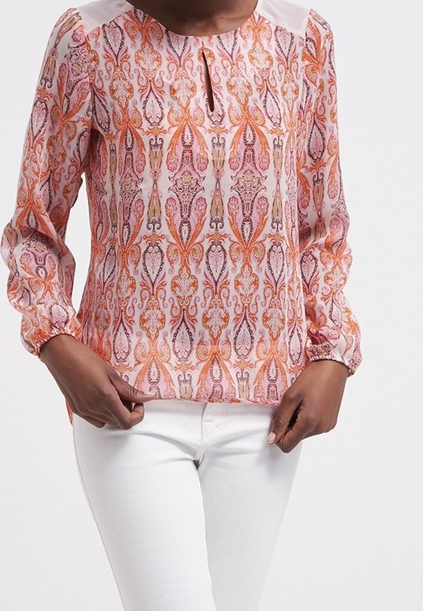 Långärmad blus med nyckelhålsöppning, prydd med ett rosa och orange blommönster på en ljus bakgrund. Tillverkad av mjukt tyg.