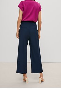 Pantalon large bleu marine avec une texture lisse, taille haute et poches arrière, associé à un top à manches courtes fuchsia.
