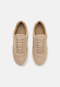 Beige suede sneakers with lacing, rounded toe, and white rubber sole. Subtle stitching details and soft texture throughout.