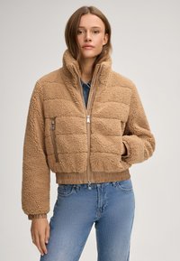 Brązowa kurtka z imitacji futra z wysokim kołnierzem, zamkiem z przodu i ściągaczami przy mankietach. Posiada pikowany wzór oraz boczną kieszeń na zamek.