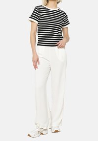 Gestreiftes Kurzarm-T-Shirt in Schwarz und Weiß, kombiniert mit weißen, weiten Hosen und weißen Sneakers, mit entspannter Passform und glatter Textur.