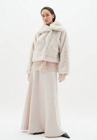 Faux päls kort jacka i off-white med matchande mjuk tröja, över en golvlång beige satängkjol och svarta spetsiga ballerina.