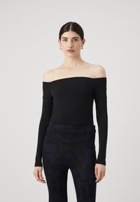 Zwarte off-the-shoulder top met lange mouwen van rekbare stof, gecombineerd met geribde marineblauwe broeken met een subtiel patroon en textuurelementen.