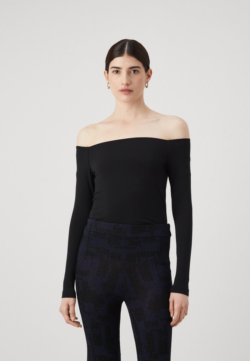 Zwarte off-the-shoulder top met lange mouwen van rekbare stof, gecombineerd met geribde marineblauwe broeken met een subtiel patroon en textuurelementen.