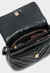 Borsa a tracolla in pelle nera trapuntata con chiusura dorata, apertura a pattina che rivela tasca interna con zip e fodera rosa chiaro.