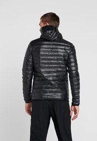 Schwarze Pufferjacke mit glänzender, strukturierter Oberfläche. Verfügt über eine Kapuze und gestickte horizontale Linien zur Isolation. Leicht und körpernah geschnitten.