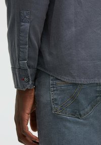 Graues Langarmhemd aus strukturiertem Stoff mit einem kontrastierenden glatten Bund, kombiniert mit blauen Jeans aus Denim mit einer Taschenakzentuierung.