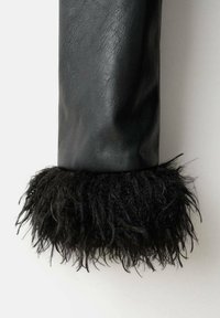 Mâneca neagră din piele cu o margine pufoasă din blană neagră texturată la manșetă, având o finisare netedă și un design curat.