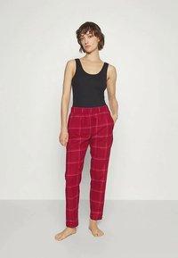 Raudonos tartano kelnės su elastine juosta ir šoninėmis kišenėmis, derinamos su juodu marškinėliu be rankovių, eksponuojamos prieš neutralų foną.