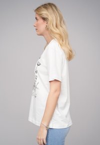 T-shirt en coton blanc à manches courtes, avec un imprimé floral noir sur le devant. Coupe classique, texture lisse et décolleté ras du cou.