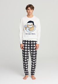 Felpa bianca a maniche lunghe con stampa di un bradipo e testo "ALTRE CINQUE MINUTI", abbinata a pantaloni in flanella a quadretti bianco e nero.