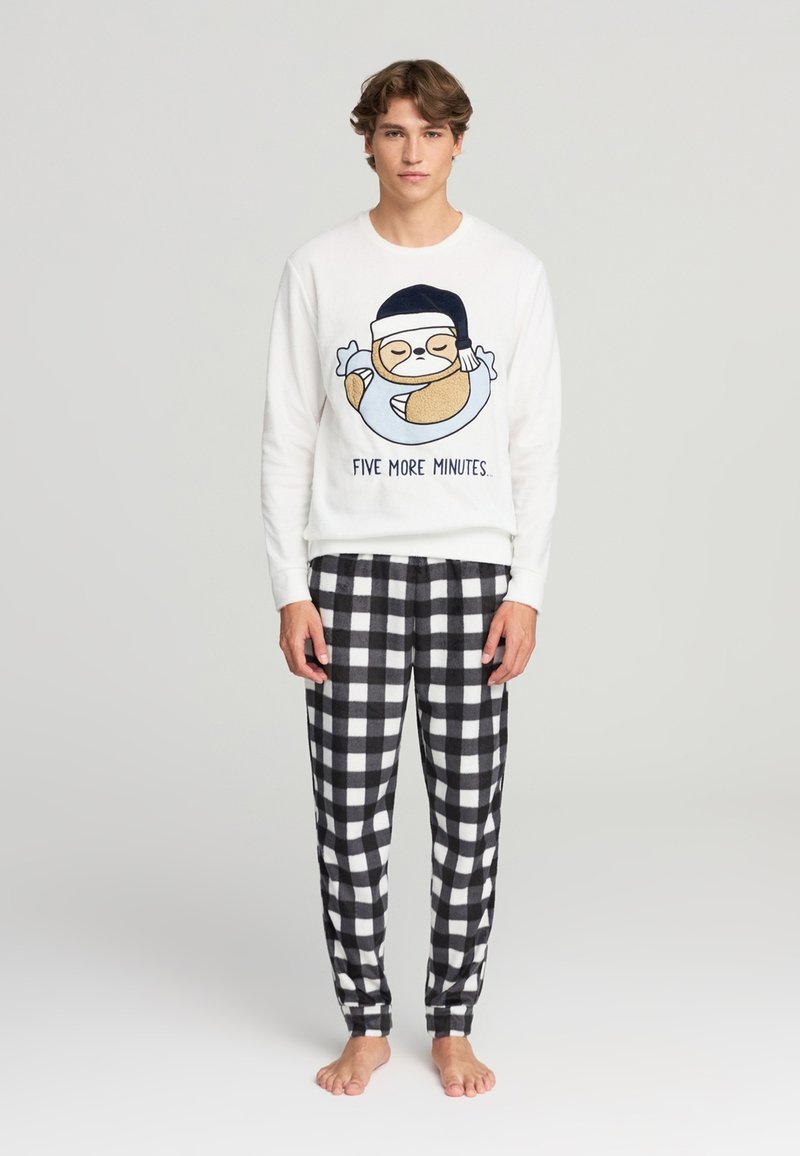Felpa bianca a maniche lunghe con stampa di un bradipo e testo "ALTRE CINQUE MINUTI", abbinata a pantaloni in flanella a quadretti bianco e nero.