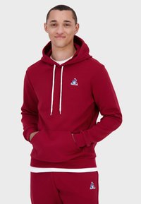 Felpa bordeaux con tasca a marsupio e lacci bianchi, dotata di un piccolo logo blu sul petto. Tessuto di cotone liscio, vestibilità comoda.