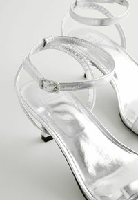 Söljstrumpade högklackade sandaler med metallisk finish, med en ankelrem och en liten blockklack. Slät struktur, minimalistisk design.