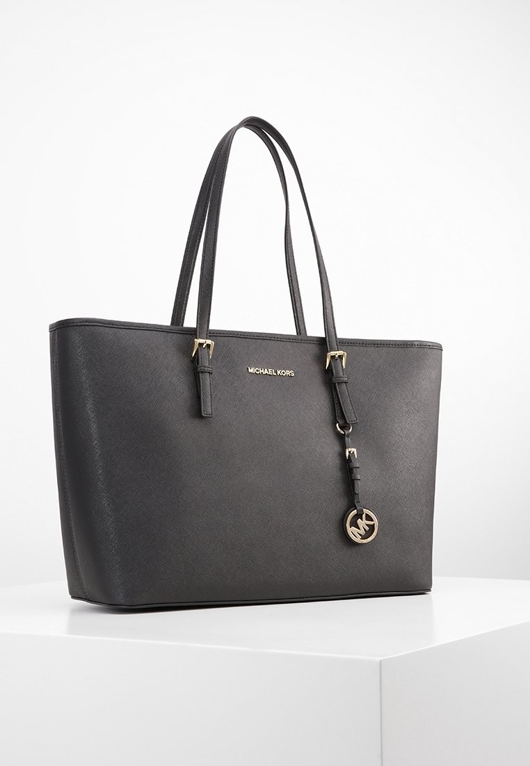 Sac cabas en cuir noir Michael Kors avec doubles anses d'épaule et breloque ronde dorée avec logo MK, présenté sur une surface blanche.