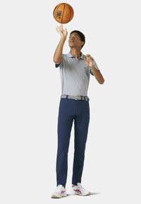 Grijze polo met kraag, navy broek, met een patroon riem en witte sportschoenen. De persoon houdt een basketbal vast.