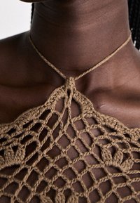 Vêtement au crochet en fil marron avec des motifs complexes, présentant un décolleté décoratif et de fines attaches autour du cou, texture semi-transparente.