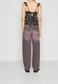 Svart blommig linne med volangade axelremmar, knytning bakom. Matchas med löst sittande, urtvättade mörklila jeans med bakfickor och synliga sömmar.