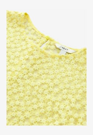 Kollane lilleline tikandiga topp, millel on õhuke kangas, ümmargune dekoltee ja tagaküljel üks nööp. Brändi silt on nähtav.