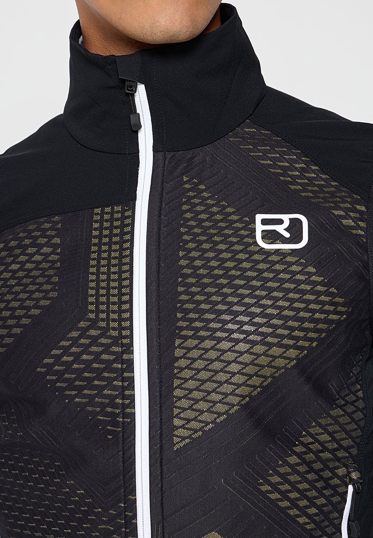 Nahaufnahme einer Person, die eine schwarze Jacke mit hohem Kragen, weißem Reißverschluss, geometrischem gelben Muster und einem weißen RJ-Logo auf der Brust trägt.