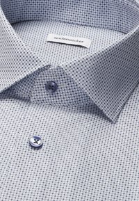 Gros plan d'un col de chemise habillée claire à motif avec des boutons foncés et une étiquette Seidensticker visible à l'intérieur du col.
