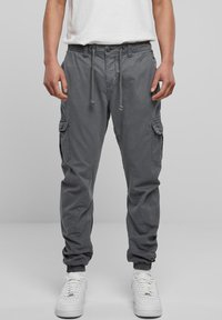 Grijze cargobroek met een elastische tailleband en trekkoord, voorzien van zijzakken en elastische boorden bij de enkels. Gekocht in combinatie met witte sneakers.