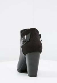 Stivaletto nero con tacco alto, realizzato con una combinazione di pelle e camoscio. Include una cerniera laterale e un dettaglio con fibbia metallica.