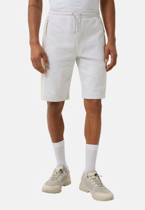 Shorts en coton gris clair avec une taille à cordon de serrage, des zips latéraux et des panneaux crème contrastants. Portés avec des chaussettes blanches et des baskets beiges.