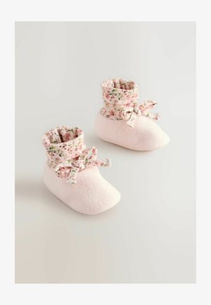 Ljusrosa fleece-sockor med en blommig mönstrad tygkant, med en rosettdetalj. Mjuk textur, rund tåform och mysig design.