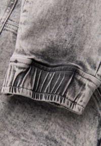 Manga de chaqueta de mezclilla gris doblada con costuras visibles y textura de la tela en vista de cerca.