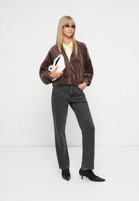 Smeđi korduroj zip-up sako s elastičnom ušicom, svijetložuta košulja s ovratnikom, crne traperice visokog struka i crne cipele s oštrom kapicom.