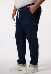 Granatowe spodnie cargo z elastycznym pasem, sznurkiem, kieszeniami bocznymi i podwiniętymi mankietami, wykonane z denimu. Noszone z białymi trampkami.