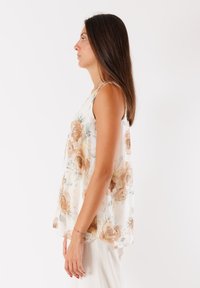 Top senza maniche in tessuto leggero e trasparente con motivi floreali beige e verdi. Vestibilità morbida con scollatura rotonda e texture morbida.