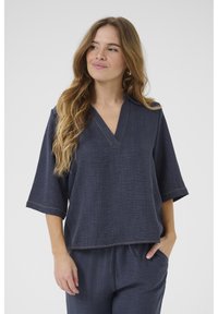 Top blu navy con scollo a V, maniche corte e vestibilità morbida. Presenta cuciture leggere lungo il collo e l'orlo. Tessuto liscio.