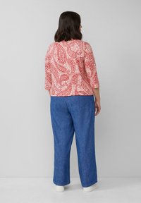 Rotes Oberteil mit Paisley-Muster und Dreiviertelärmeln, kombiniert mit lockeren blauen Jeans. Strukturiertes Material, lässige Passform und weiße Sneakers.